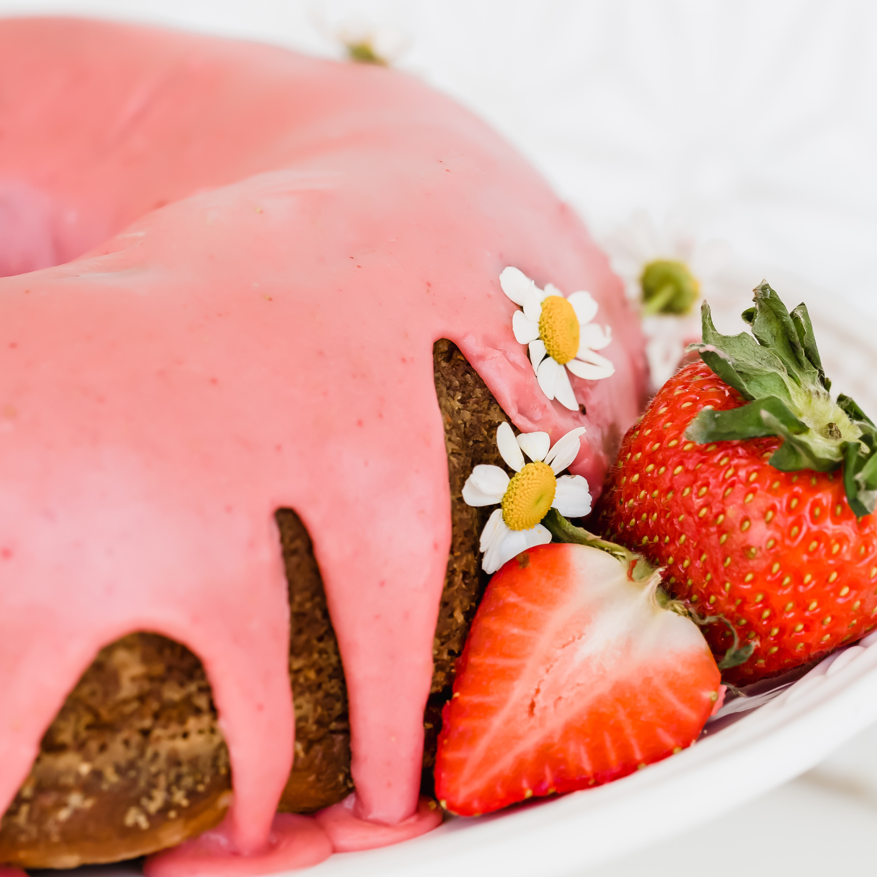 the whole strawberry bundt cake iced with fresh strawberries beside it.