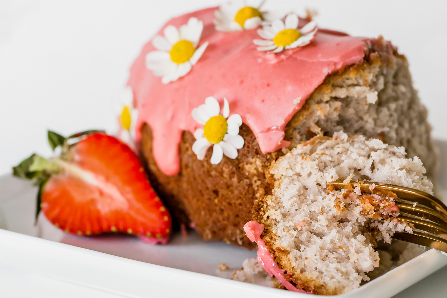 strawberry bundt cake on a white plate with a fork and a sliced fresh strawberry next to it.