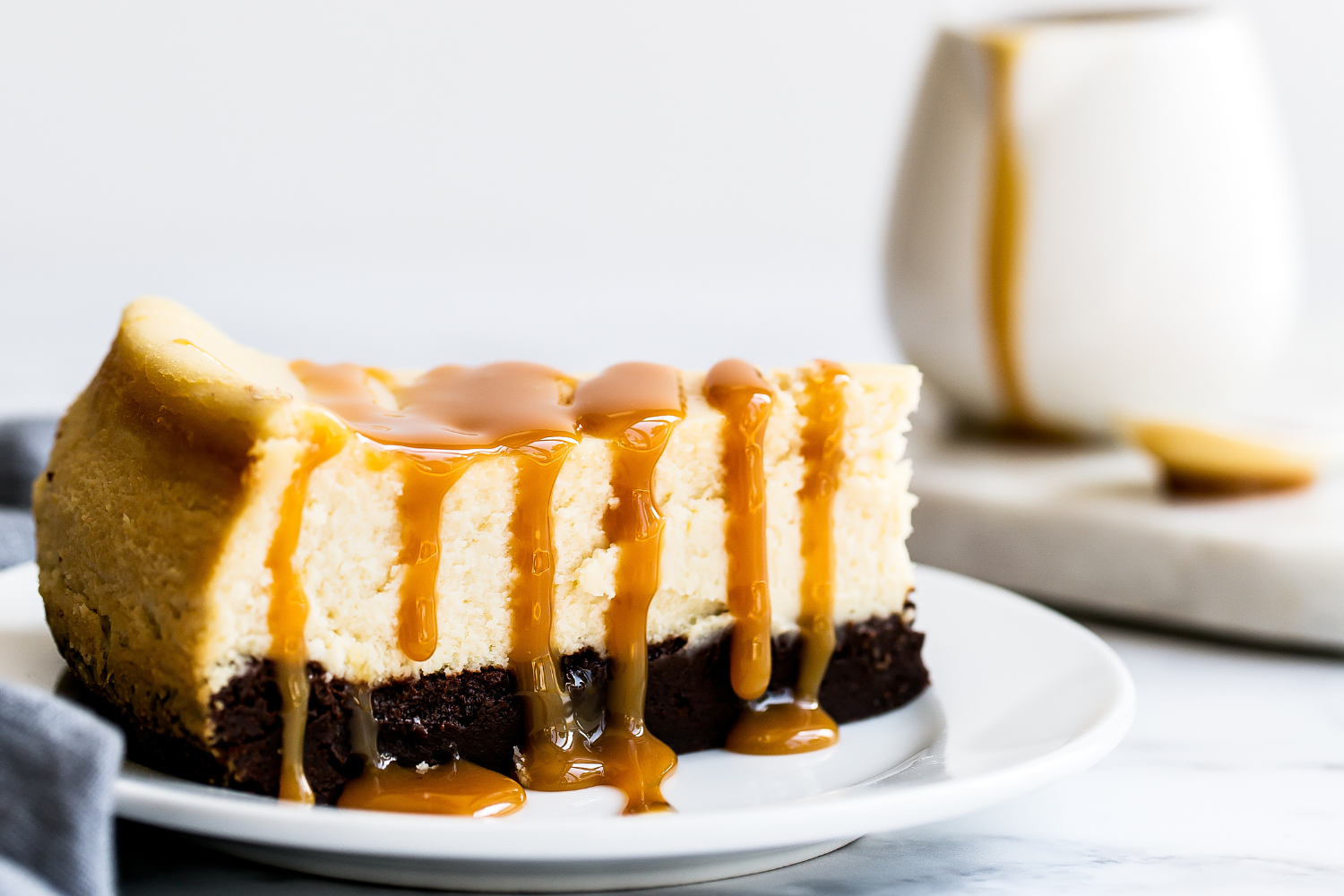 a slice of cheesecake on a plate, with salted caramel sauce drizzled over the top, dripping down the sides.