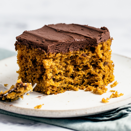 a slice of easy pumpkin cake, topped with simple whipped ganache, served on a white plate with a fork
