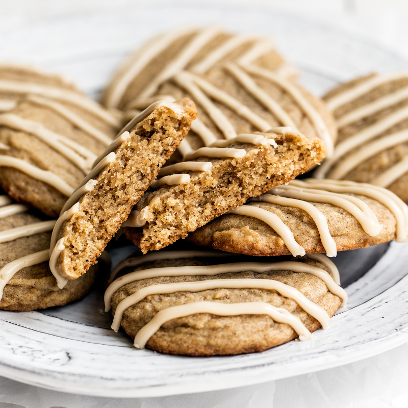 several chai sugar cookies on a plate, drizzled with lines of coffee glaze, with one broken in half to show the soft chewy interior.