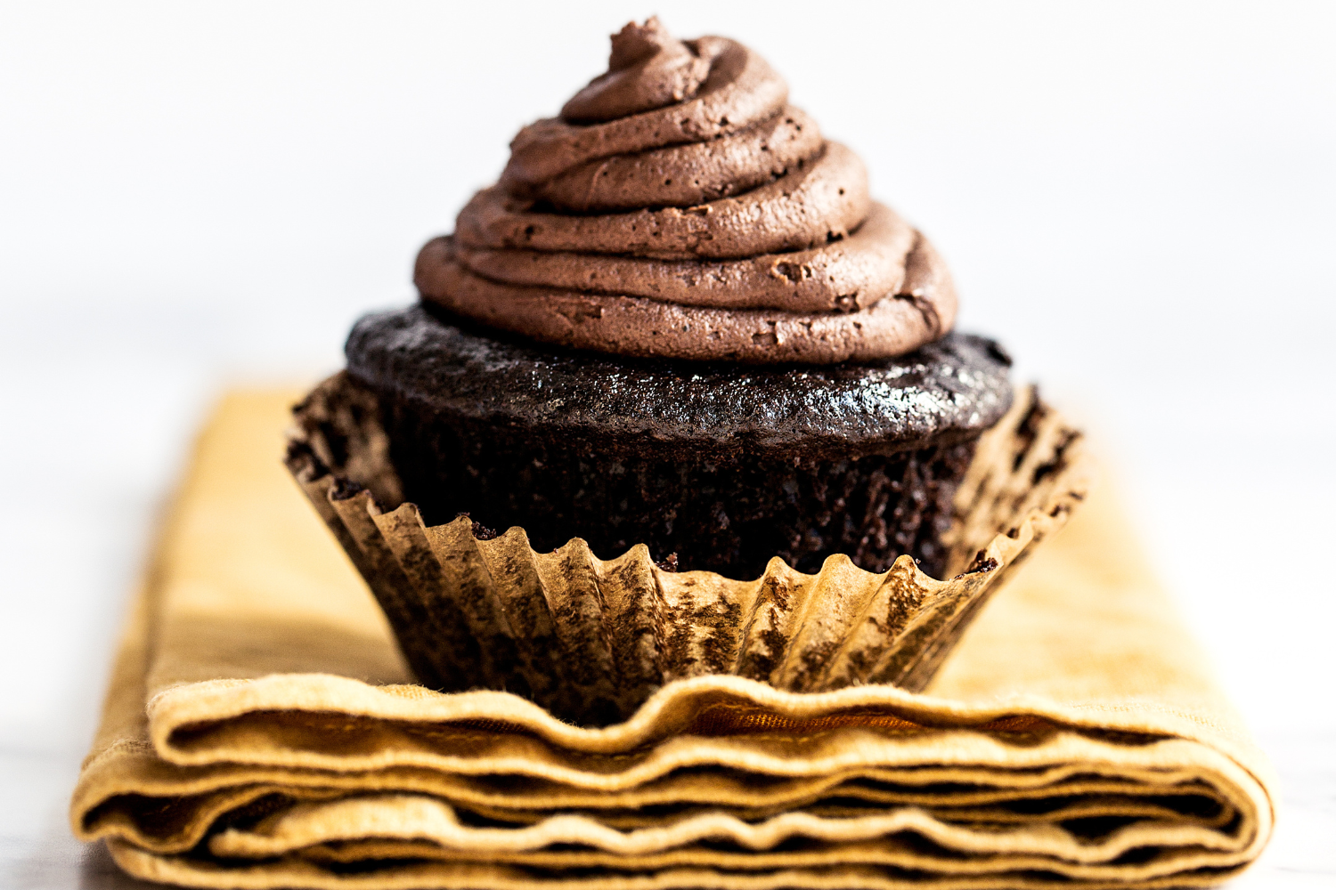 a chocolate blackout cupcake in a gold liner on top of a deep yellow napkin, ready to serve.