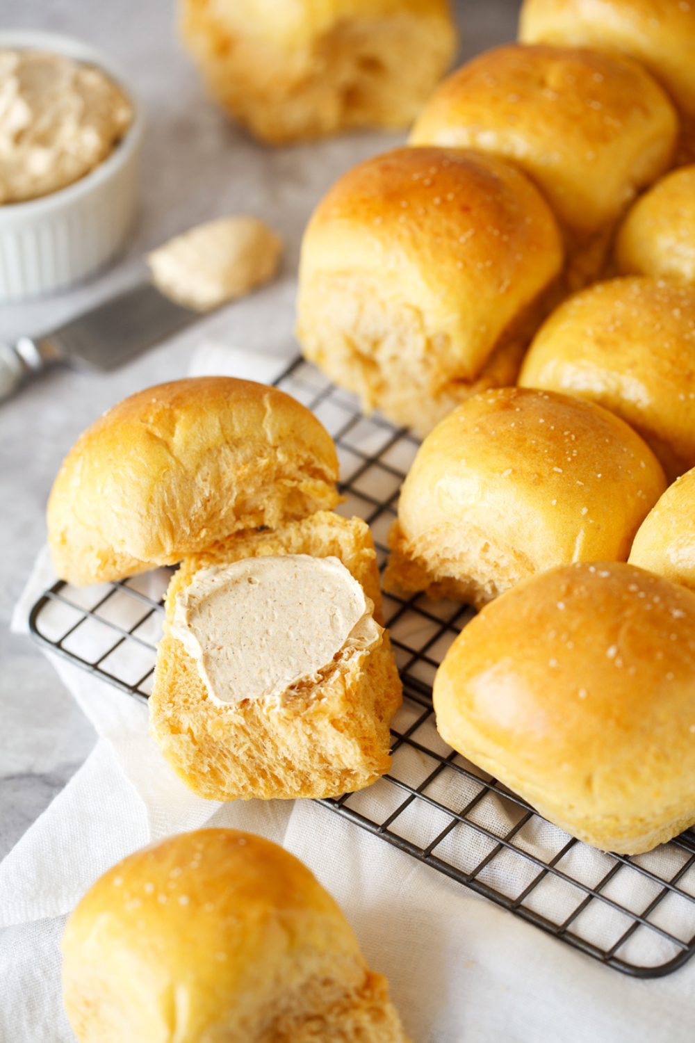 sweet potato dinner rolls on a cooling rack, with one cut open and slathered with butter to serve.