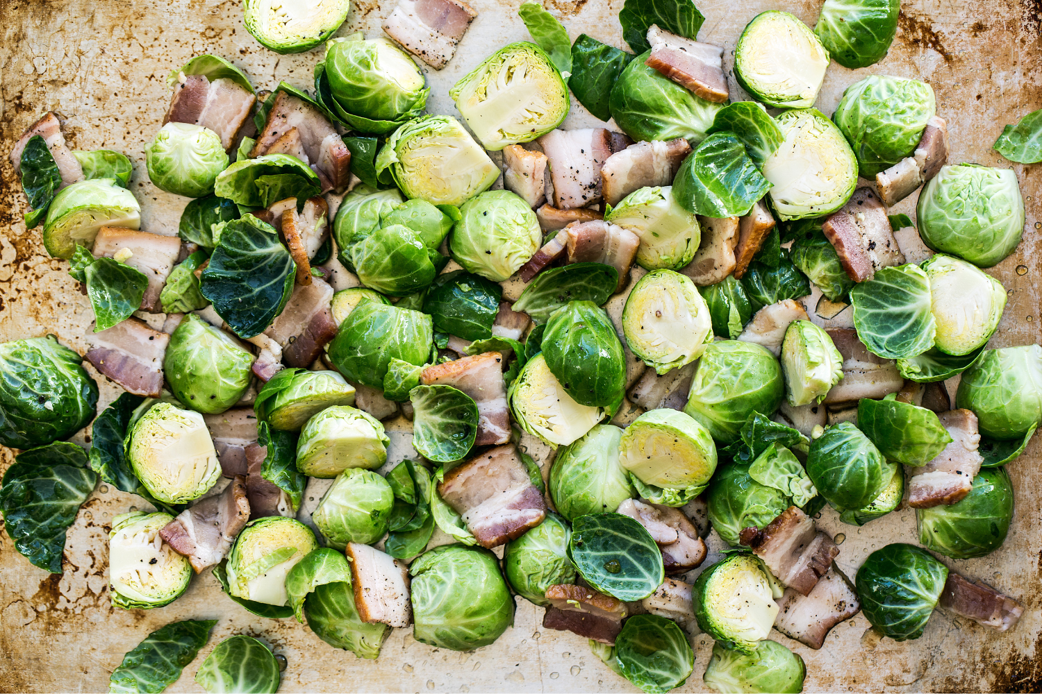 the uncooked halved Brussels sprouts and diced bacon on a baking tray, ready to bake.