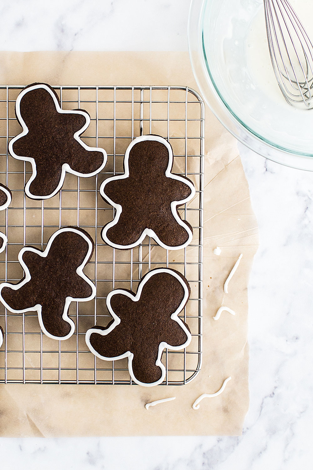 Gingerbread Men Cookies on a cooling rack, with white icing being piped on.