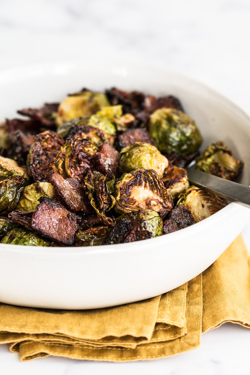 a white ceramic bowl filled with Maple Bacon Brussels Sprouts and a spoon, ready to serve.