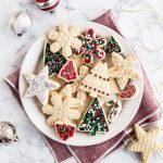 a plate of pretty cut-out sugar cookies on a plate, with a red napkin behind and a couple ornaments placed around.
