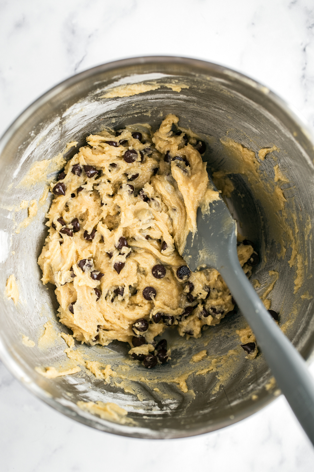 Thin and crispy chocolate chip cookie dough in a metal bowl with a spatula