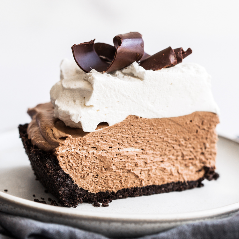a perfect slice of French silk pie with whipped cream and chocolate curls on top, on a plate, ready to serve.