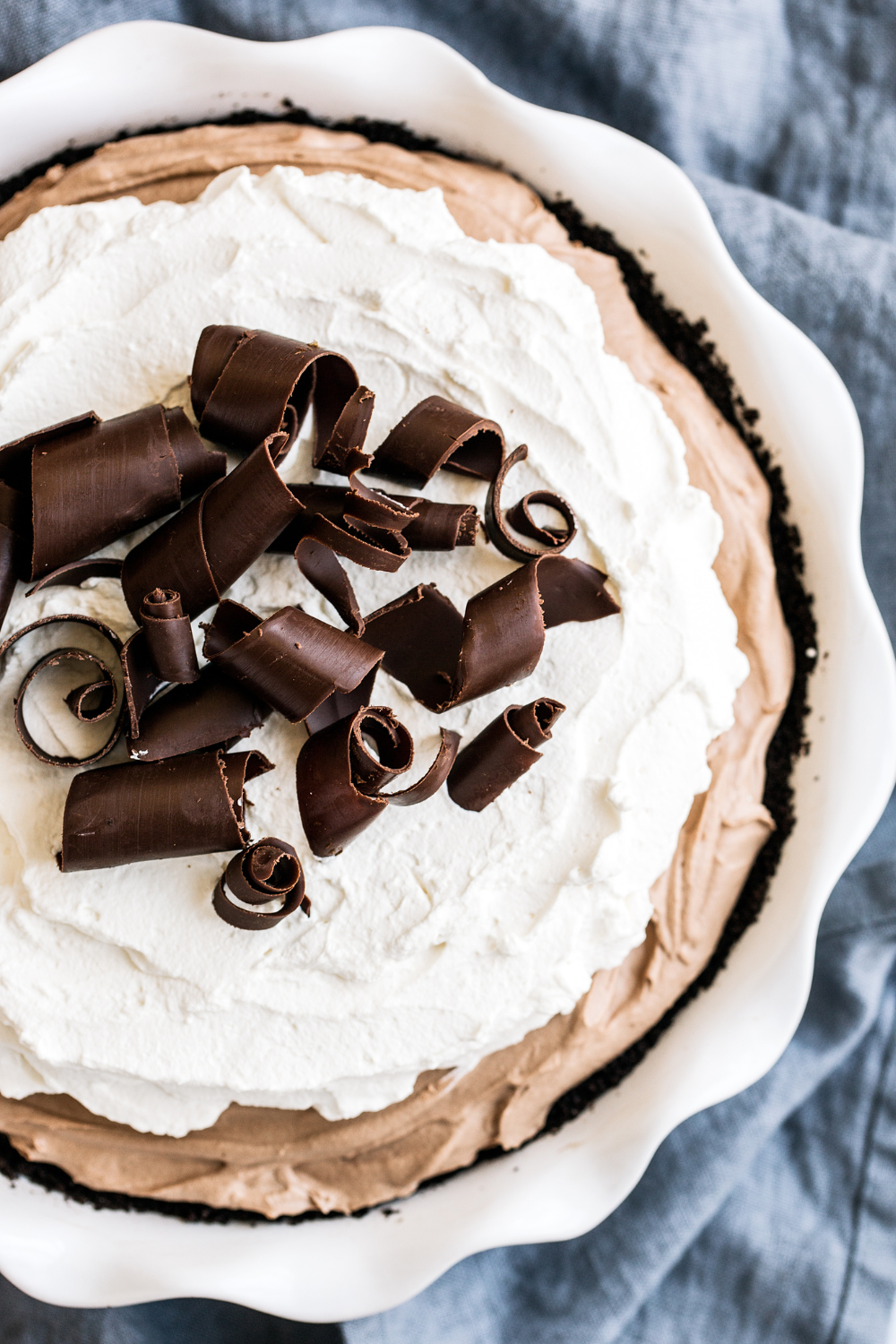 French Silk Pie with whipped cream and chocolate curls on top, in a ceramic pie pan.