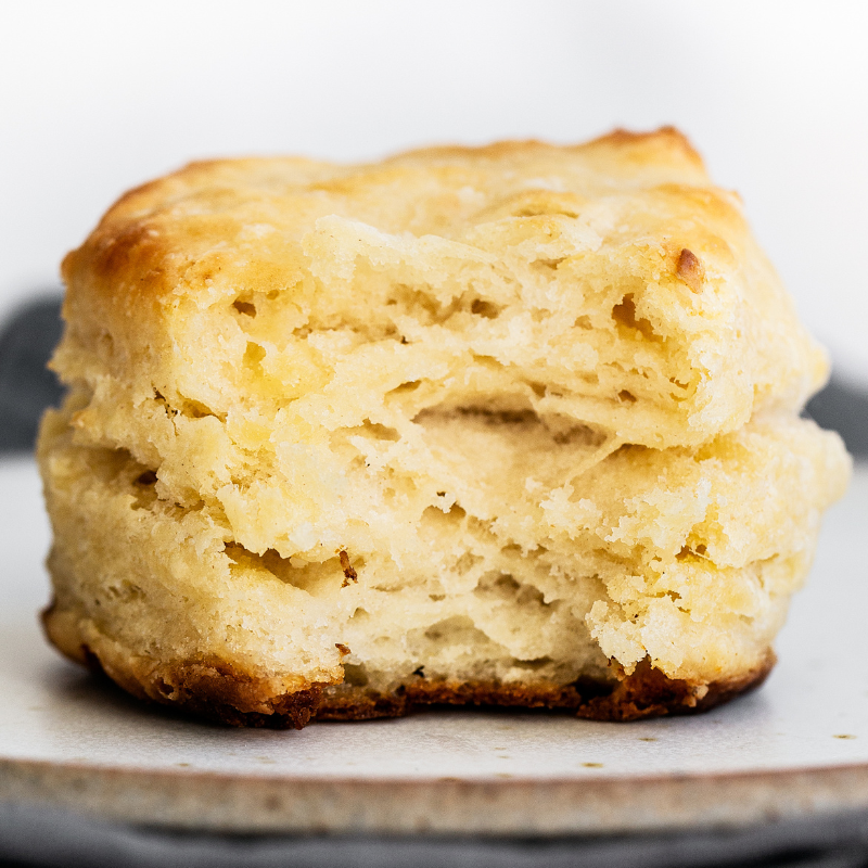 buttermilk biscuit sitting on a plate, with a bite taken out to show the flaky, tender, layered interior