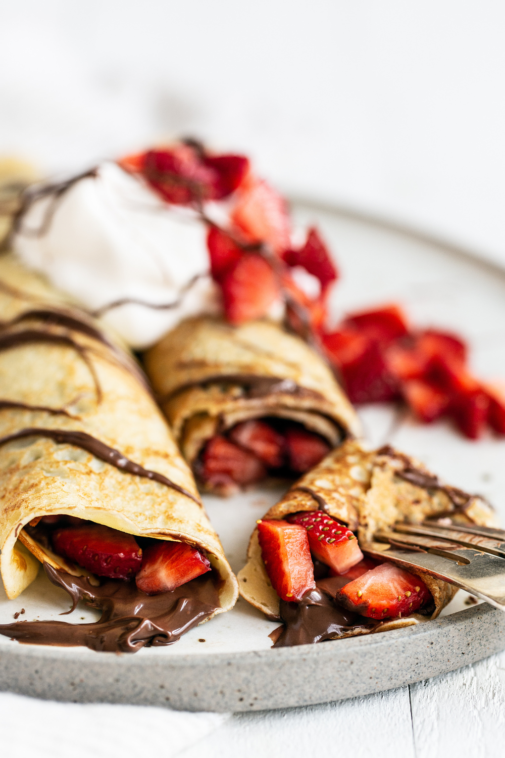 two rolled crepes filled with chocolate and fresh strawberries, with a piece on a fork ready to enjoy.