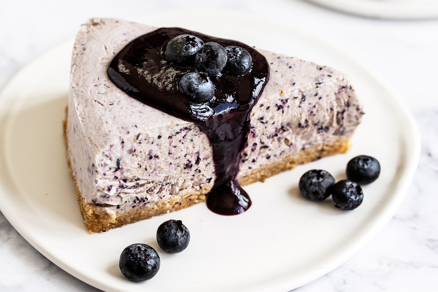 one slice of blueberry frozen pie on a white plate, drizzled with blueberry sauce on top.