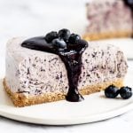 a slice of blueberry frozen pie on a white plate, with a few fresh blueberries next to the pie and a drizzle of blueberry sauce on top.