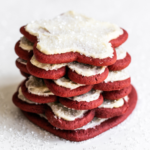 a stack of red velvet cut out cookies with cream cheese frosting.