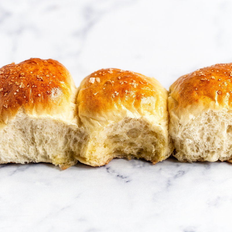 three buttery dinner rolls in a row, the middle one with a bite taken out.