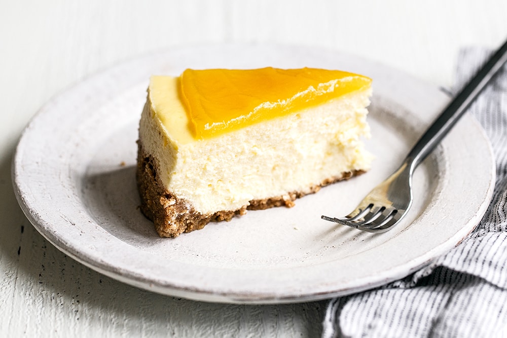 Slice of homemade lemon cheesecake with graham cracker crust on a plate with a fork