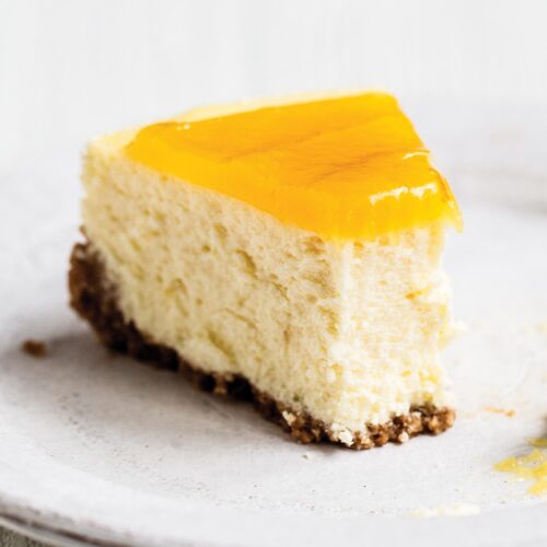 Slice of homemade lemon cheesecake with graham cracker crust on a plate with a fork