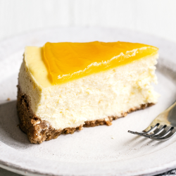 a slice of cheesecake topped with lemon curd, on a plate with a fork.