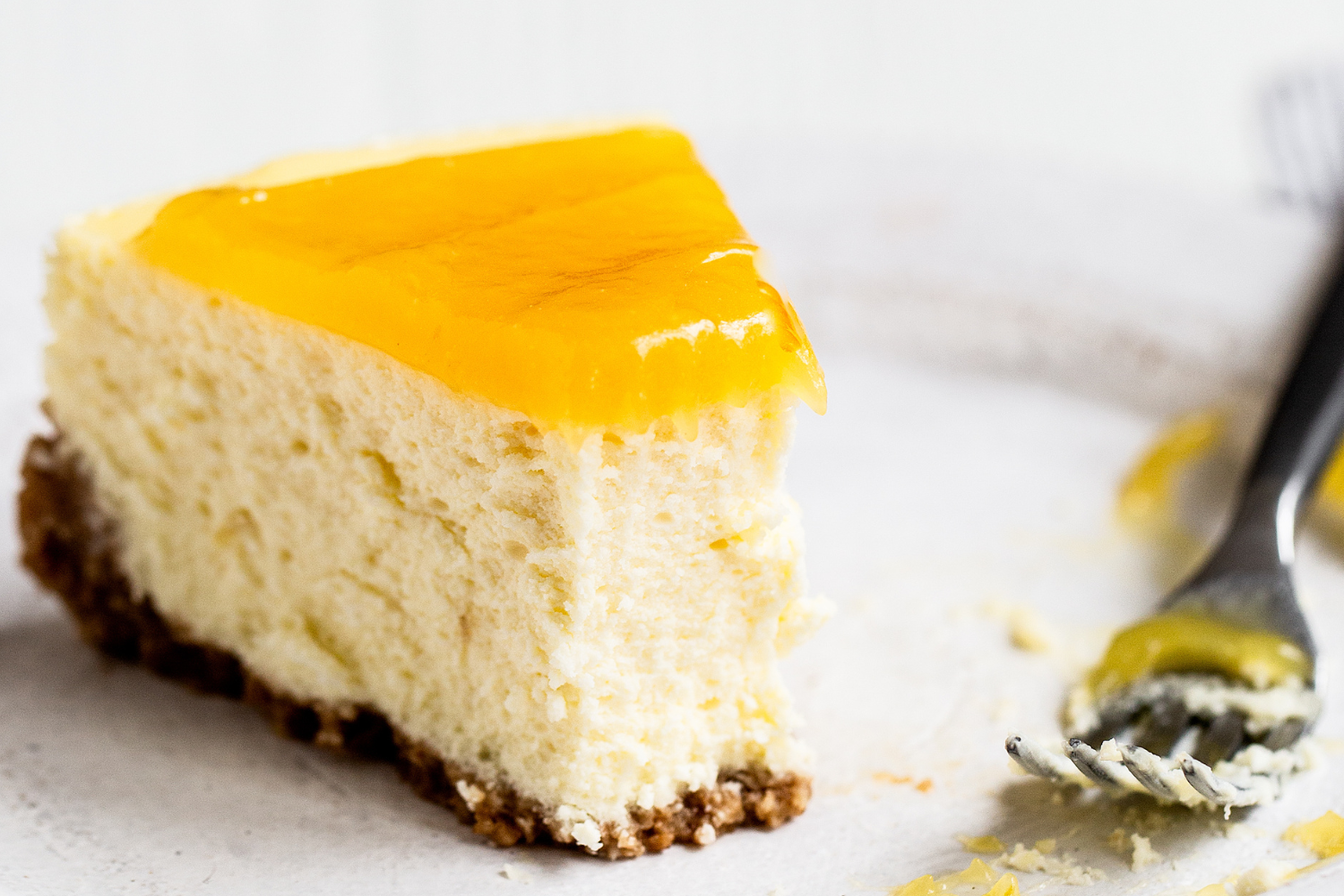 a slice of lemon cheesecake on a plate, with a fork and a bite being taken out.