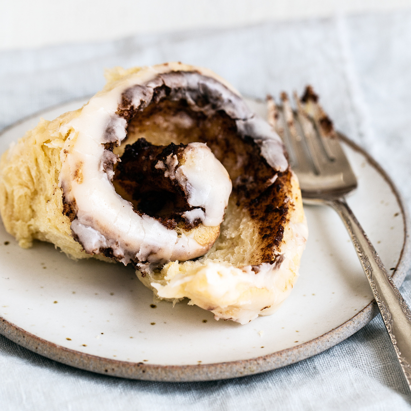 gooey cinnamon roll on a plate with a fork, ready to enjoy