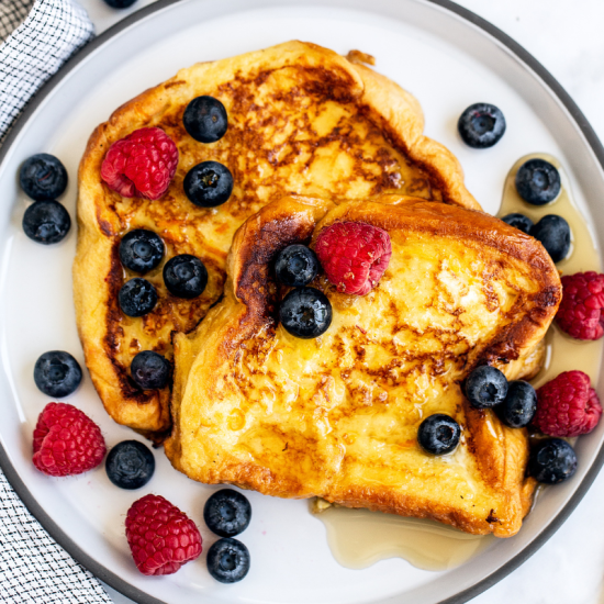 perfect French toast slices sitting on a plate, with a little maple syrup and some fresh berries on the plate