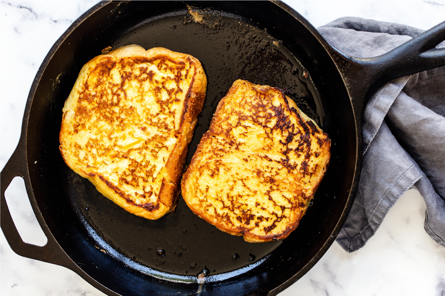 two slices of French toast in a skillet, cooking before serving