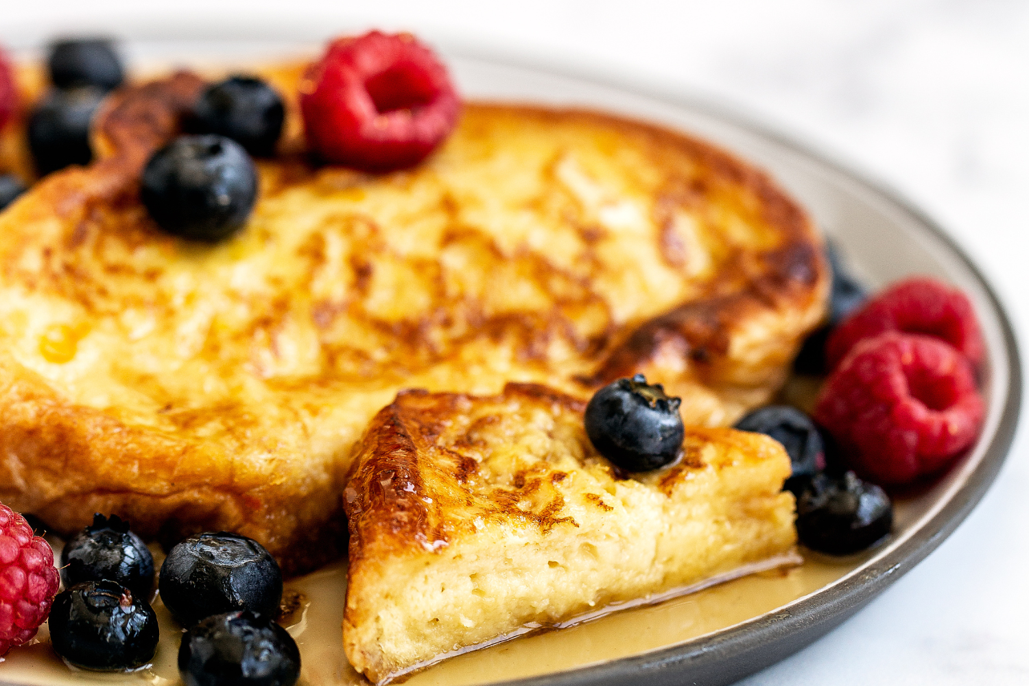 slices of golden brown French Toast, with some maple syrup and fresh berries, on a plate ready to serve