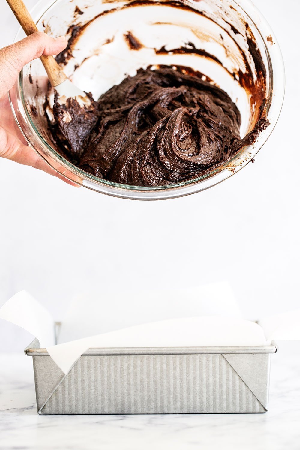 Dark chocolate brownie batter going into metal baking pan