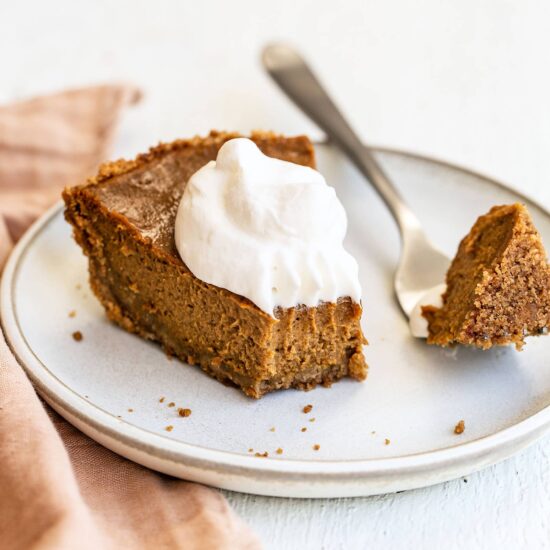 Slice of easy pumpkin pie with graham cracker crust and whipped cream on top