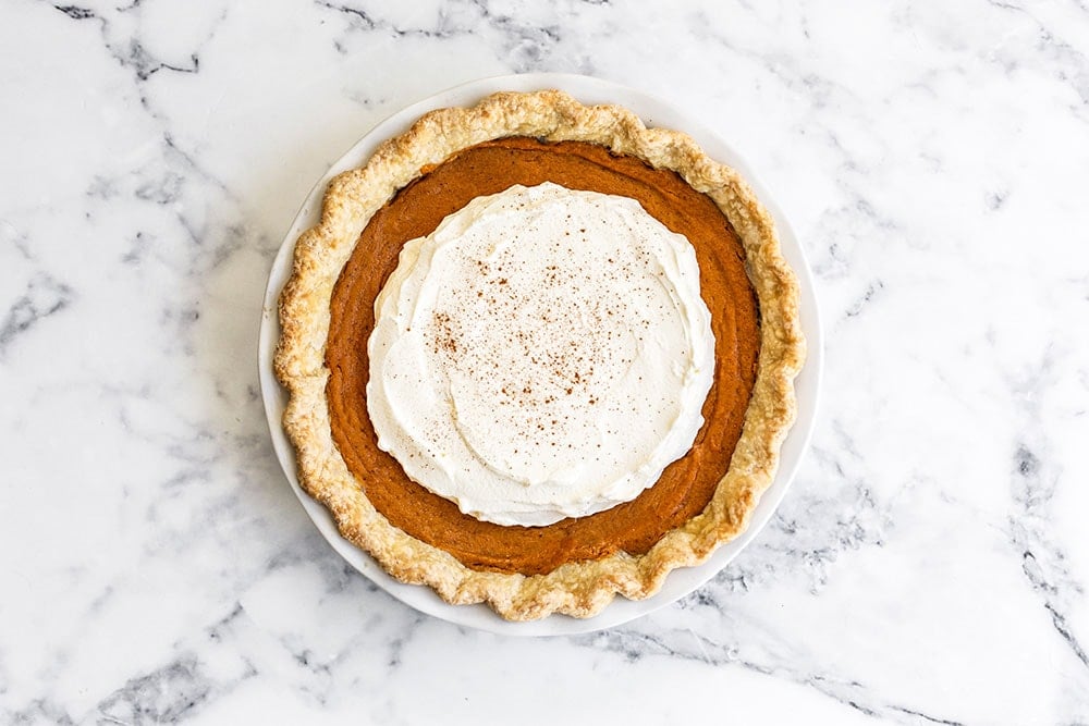Brown butter sweet potato pie with whipped cream on a marble counter