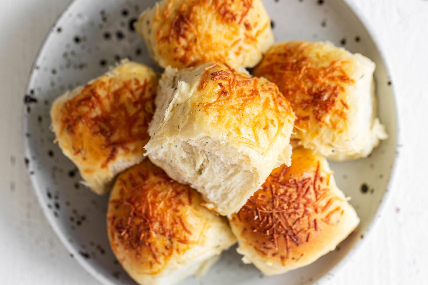 a pile of garlic herb cheese dinner rolls on a plate, ready to serve.