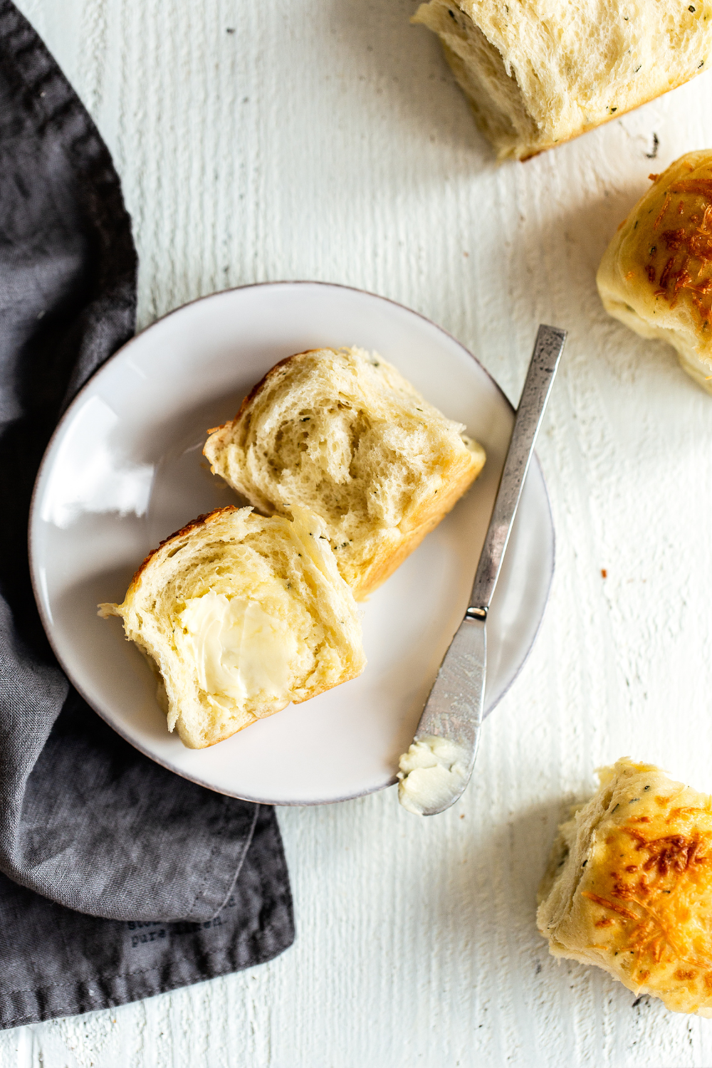 a garlic herb cheese dinner roll recipe split open on a plate, slathered with butter, before serving.
