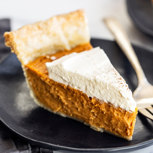 a perfect slice of brown butter sweet potato pie, with whipped cream on top, sitting on a black plate with a fork.
