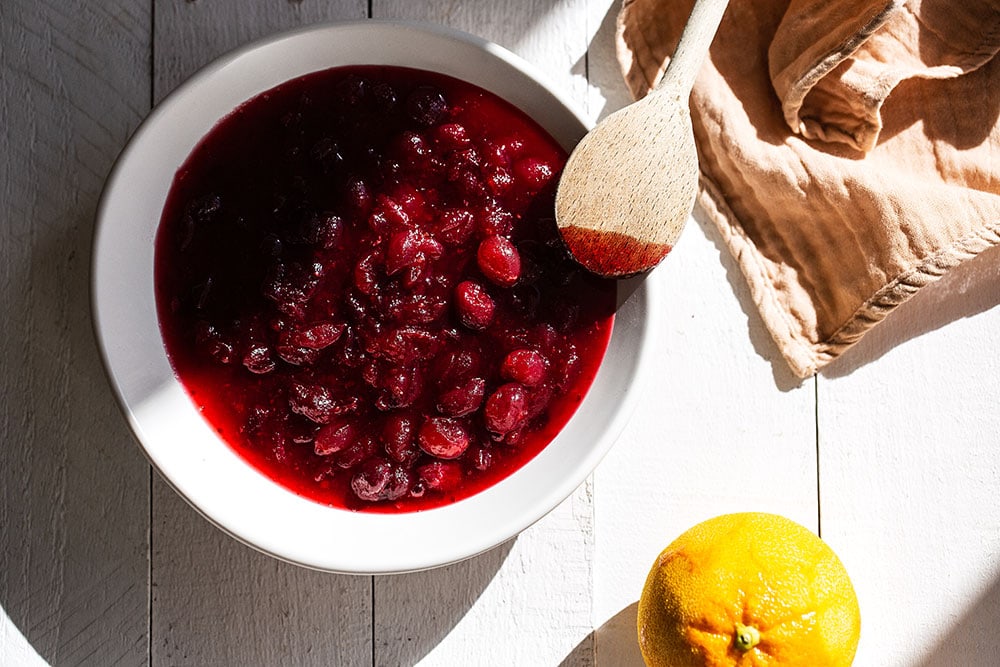 Cranberry sauce in a bowl on the table with an orange and a spoon