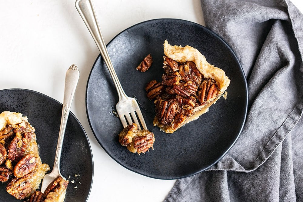 Slice of pecan pie on a plate with a fork taking a bite
