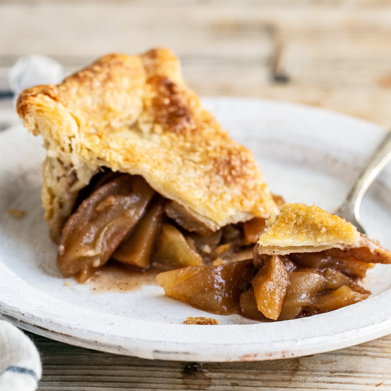 a slice of homemade apple pie on a white plate, with a fork, ready to serve.