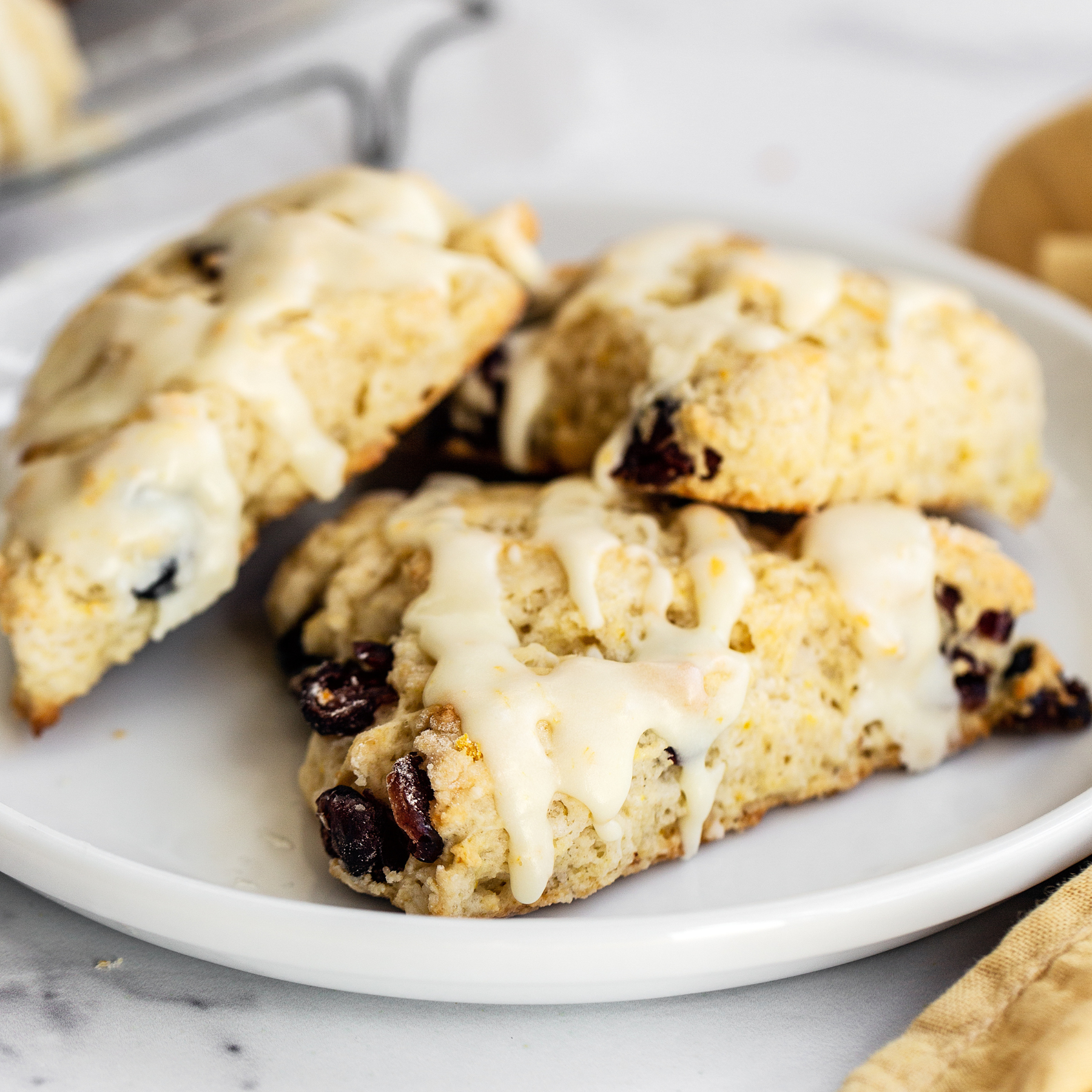 three cranberry scones drizzled with orange icing, on a white plate, ready to serve.