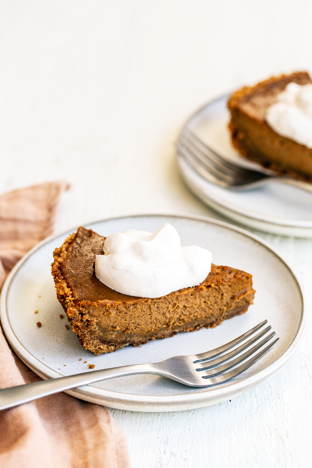 two slices of pumpkin pie with whipped cream on top, on plates,