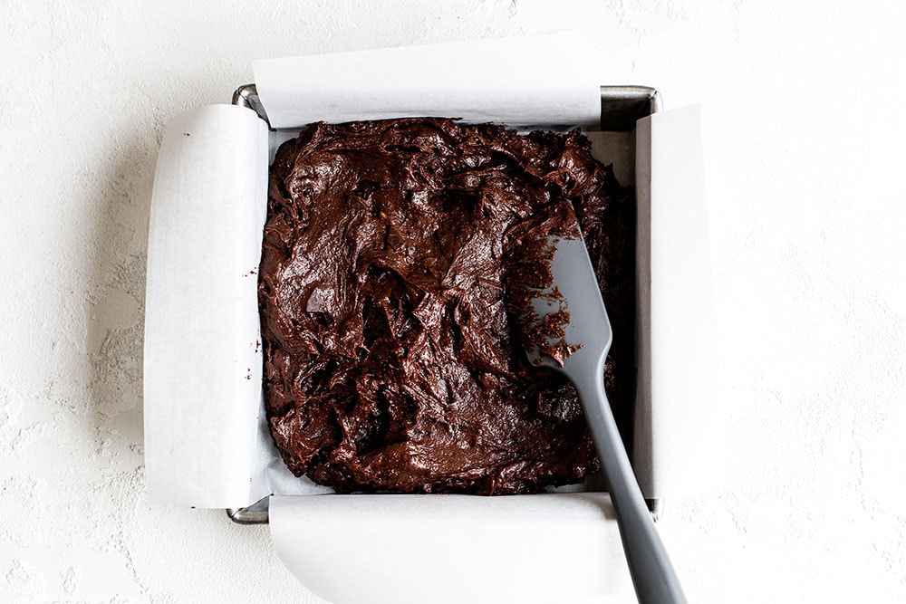 Brownie batter in a parchment lined baking pan with a spatula