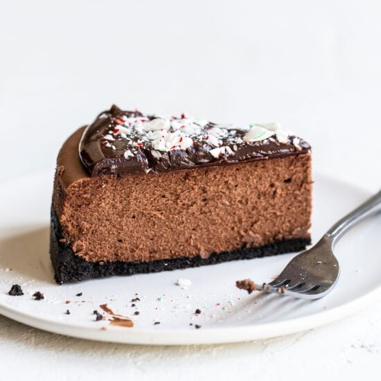 Slice of peppermint chocolate cheesecake on a plate with crushed candy canes on top