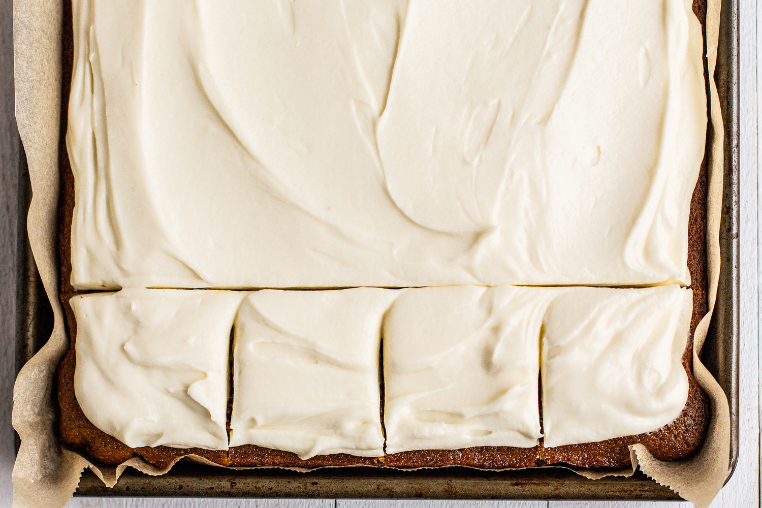 Gingerbread Sheet Cake topped with cream cheese frosting, with part of the cake sliced up to serve.