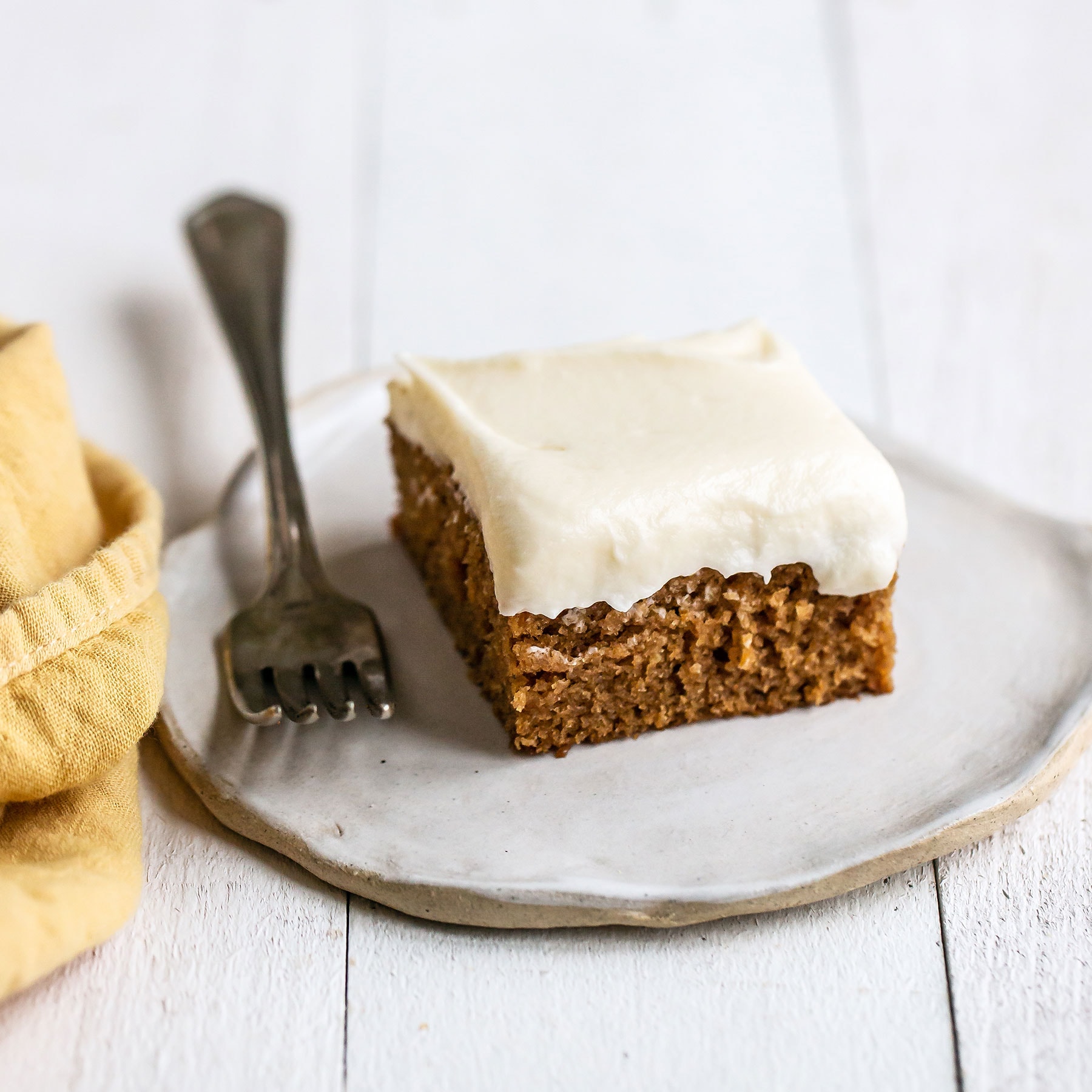 Slice of gingerbread sheet cake with cream cheese frosting on a plate