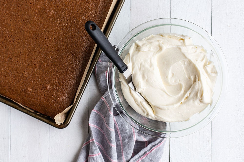 Quick gingerbread sheet cake in a pan with a bowl of cream cheese frosting next to it