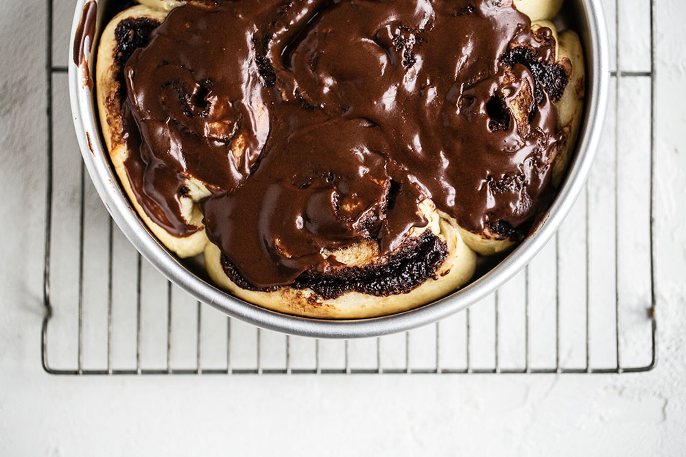 Gooey chocolate swirl rolls in baking pan with cocoa icing flooded on top
