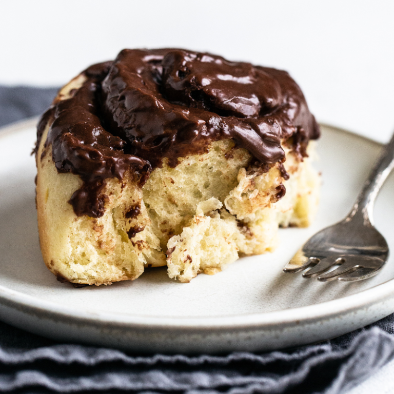 a chocolate roll covered in chocolate icing, on a plate with a fork beside it, with a bite taken out.