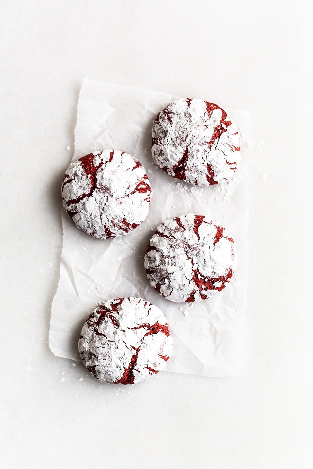 Red velvet crinkle cookies on parchment paper with a snowy coating of powdered sugar