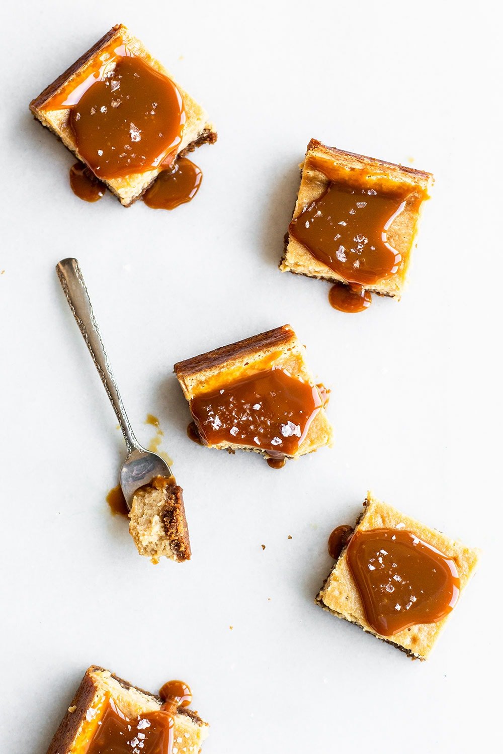 Bars of salted caramel cheesecake topped with caramel sauce and flaky sea salt