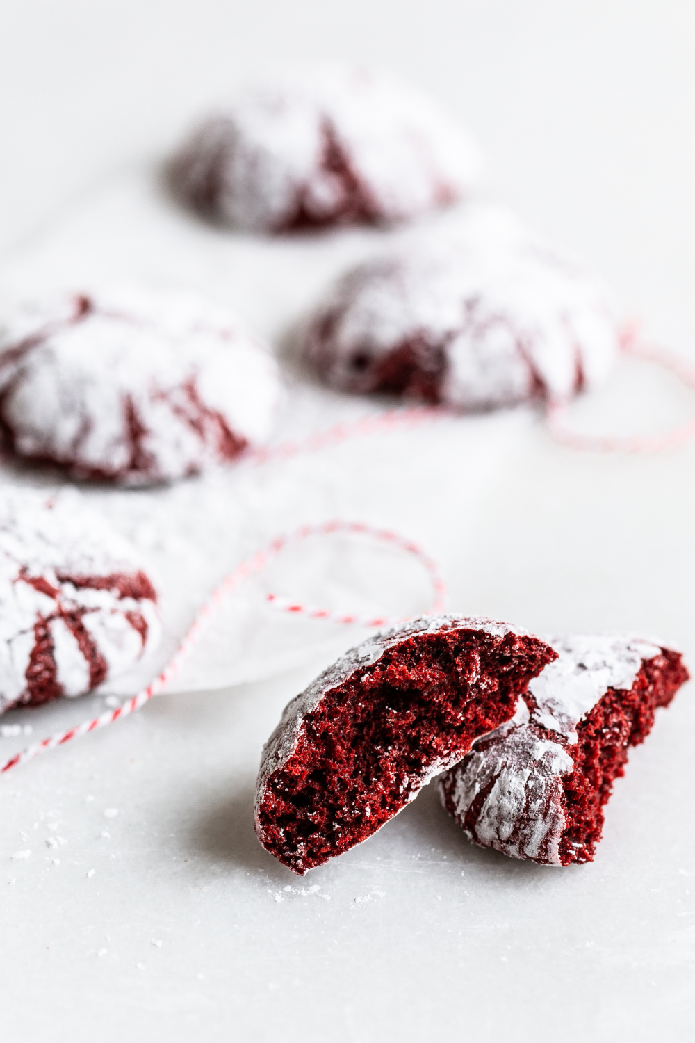 several Red Velvet Crinkle Cookies with one broken open, to show its bright red interior.