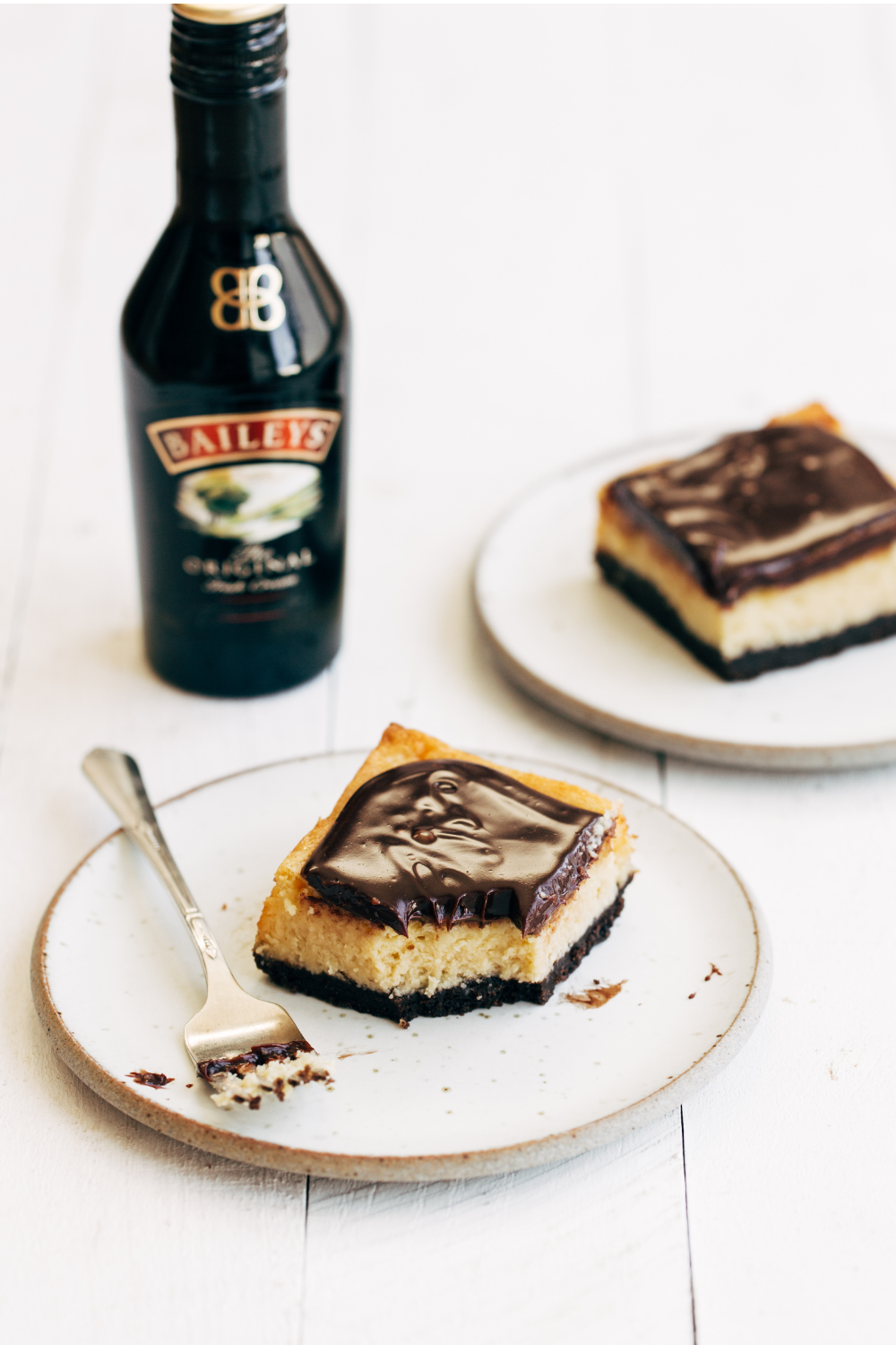 a bottle of Bailey's Irish Cream behind a couple slices of cheesecake bars on plates, ready to serve.
